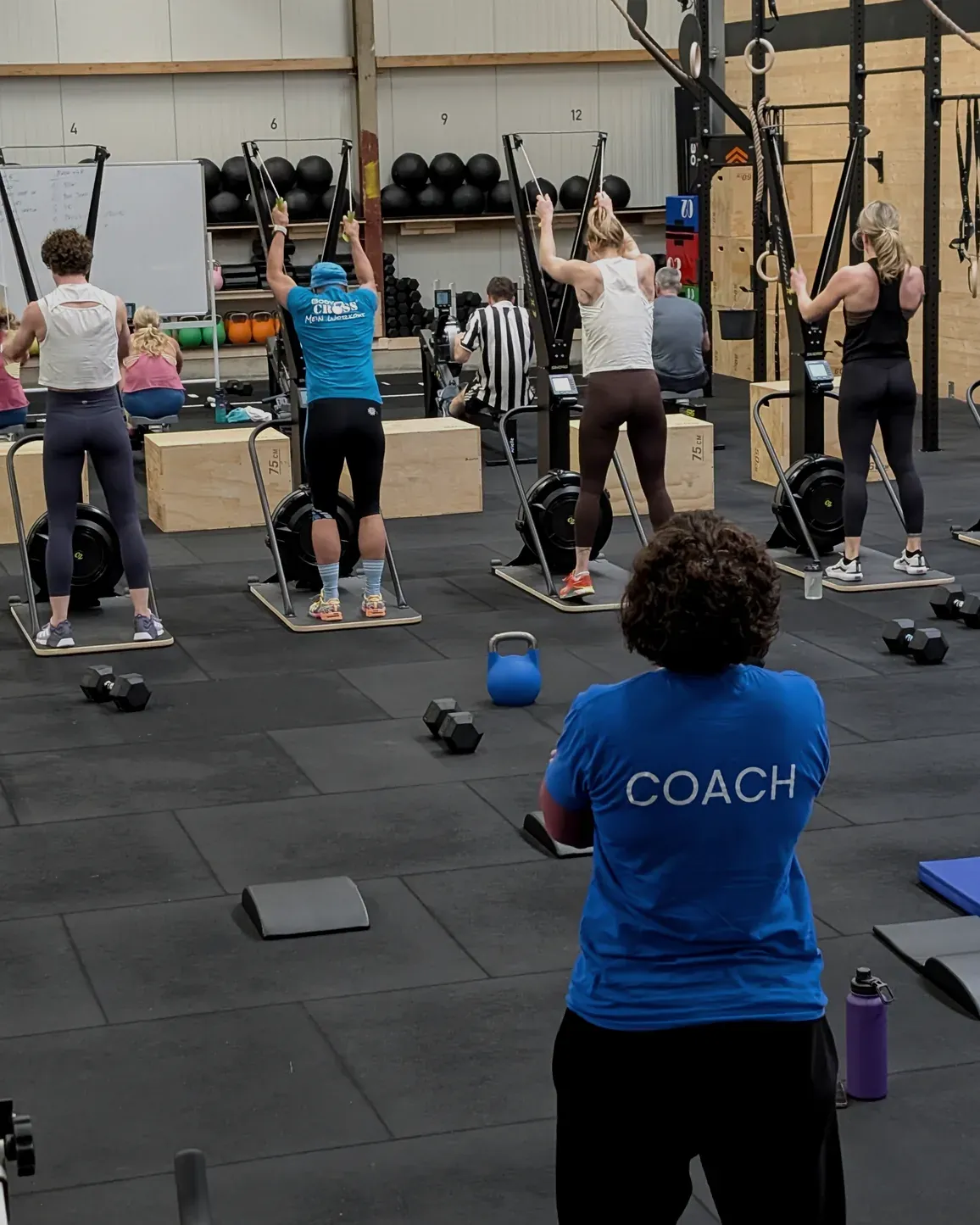 Ein Coach steht mit dem Rücken zur Kamera vor einer Class an den SkiErgs in der Halle von AMITY Athletics in Dülmen